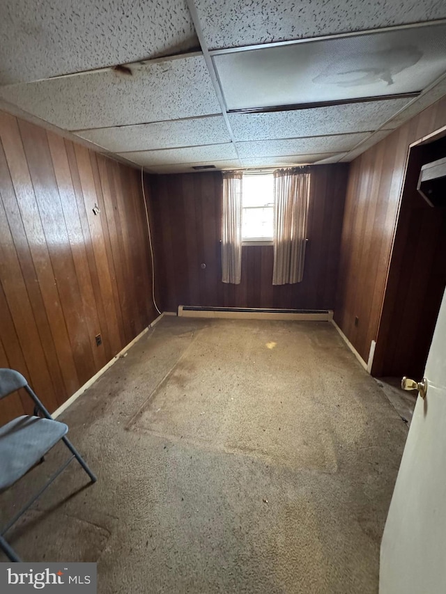 carpeted empty room featuring a drop ceiling and wood walls