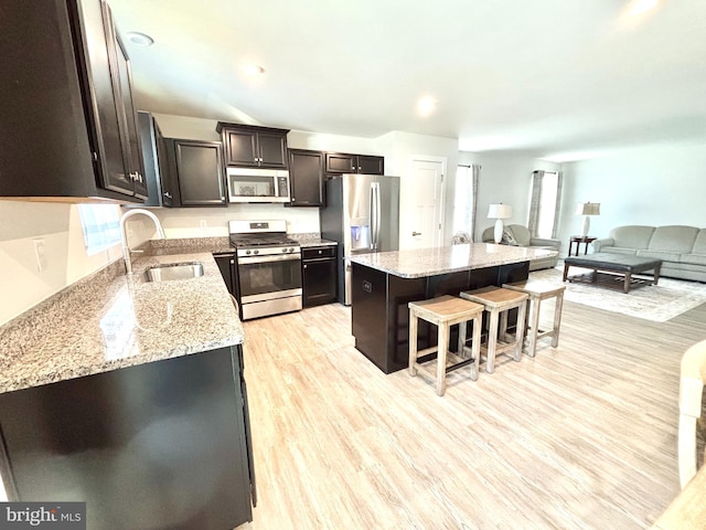 kitchen with appliances with stainless steel finishes, sink, a center island, light stone counters, and light hardwood / wood-style floors