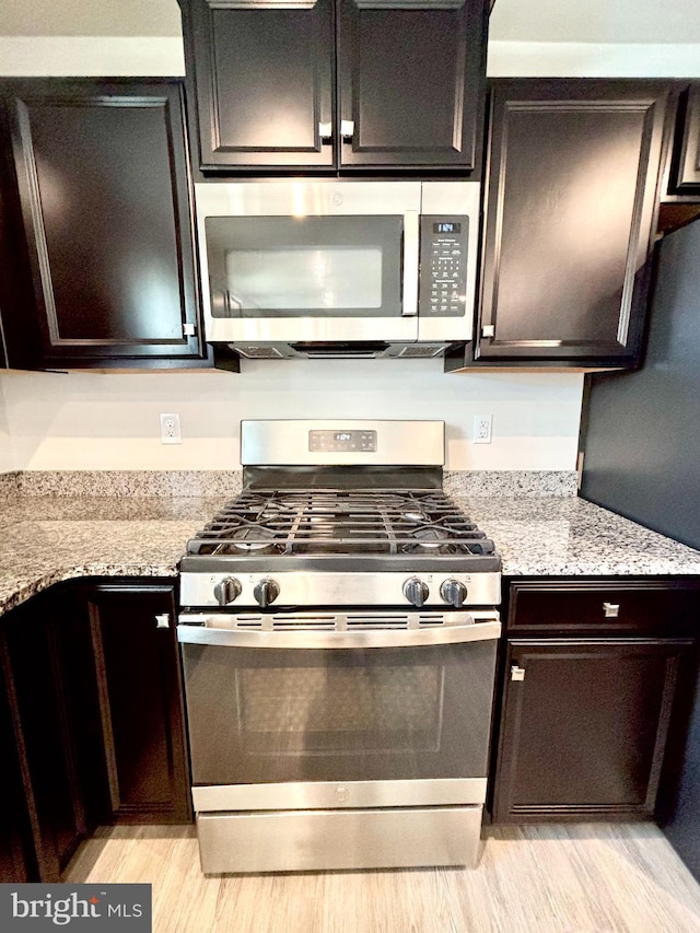 kitchen with light stone counters, light wood-type flooring, dark brown cabinetry, and appliances with stainless steel finishes