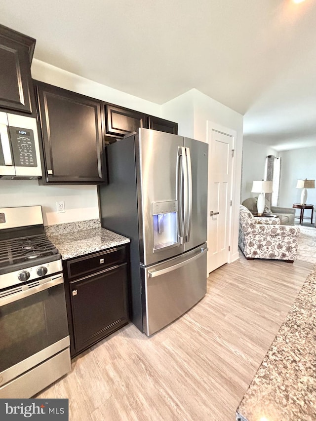 kitchen with light stone countertops, appliances with stainless steel finishes, and light wood-type flooring