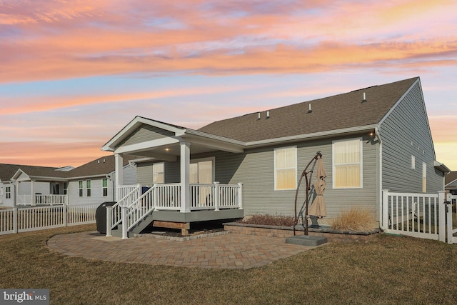 back house at dusk with a patio area and a lawn