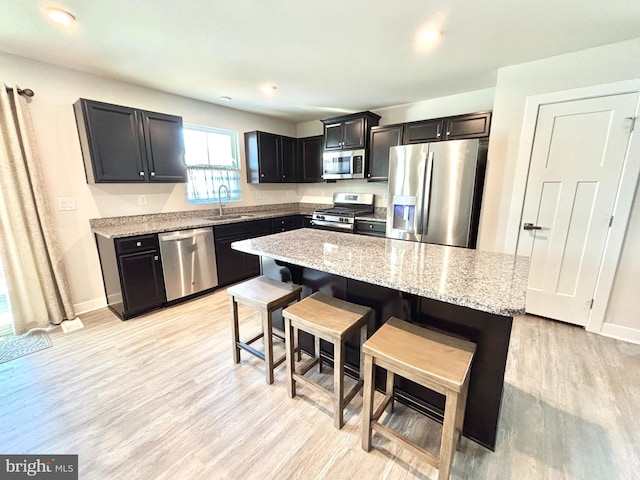 kitchen featuring sink, a kitchen breakfast bar, stainless steel appliances, a center island, and light stone countertops