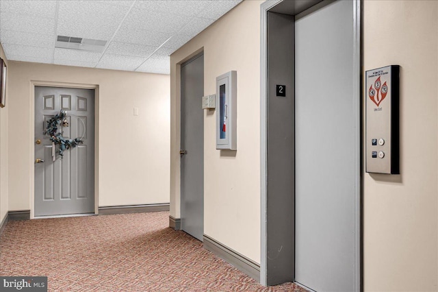 hall with a drop ceiling, elevator, and carpet