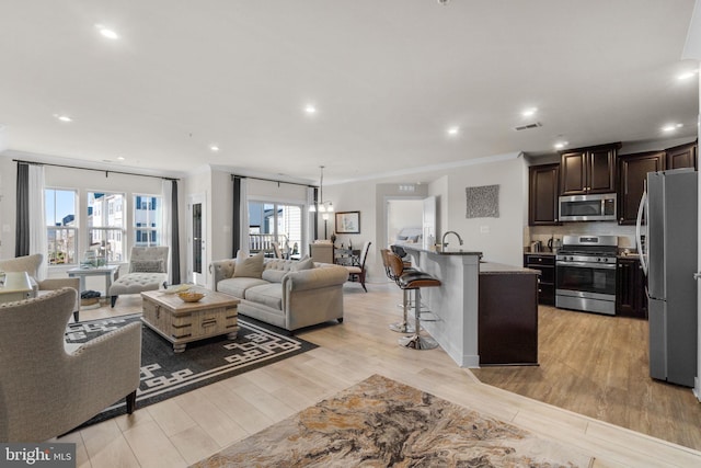 living room with ornamental molding, sink, and light wood-type flooring