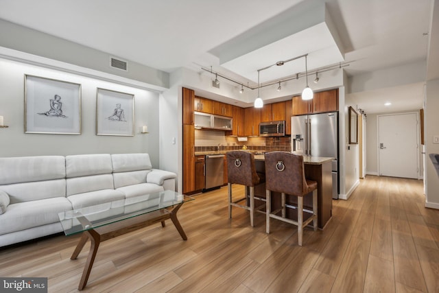 kitchen featuring appliances with stainless steel finishes, pendant lighting, a kitchen breakfast bar, light hardwood / wood-style floors, and track lighting