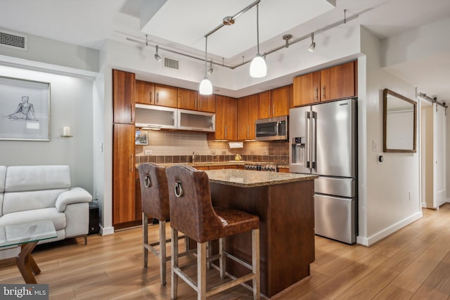 kitchen with appliances with stainless steel finishes, backsplash, hanging light fixtures, track lighting, and light wood-type flooring