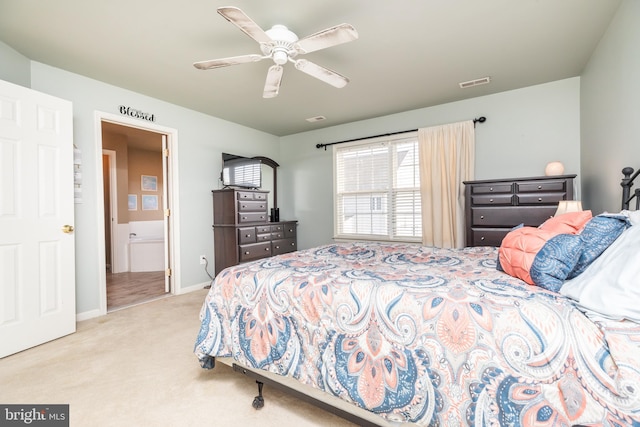 bedroom with ensuite bathroom, light colored carpet, and ceiling fan