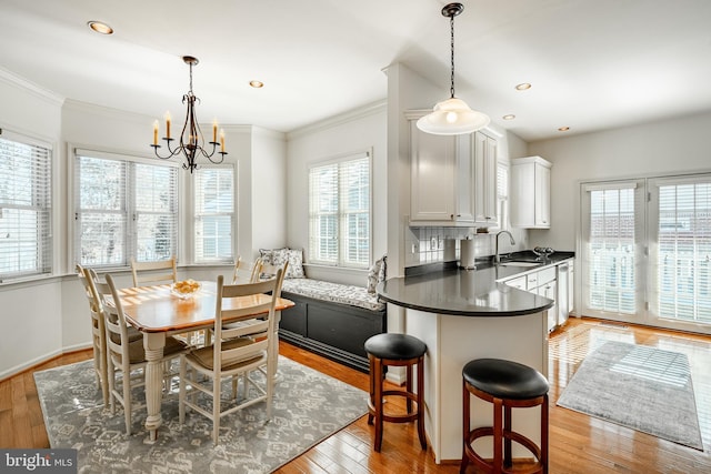 dining space with sink, a notable chandelier, light hardwood / wood-style flooring, and ornamental molding