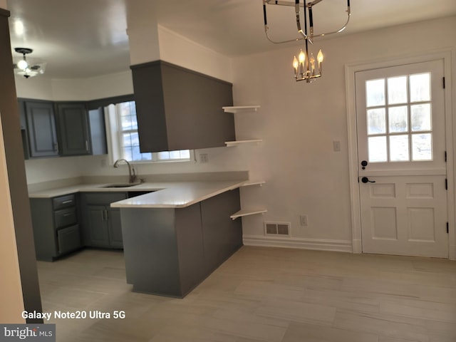 kitchen with sink, gray cabinetry, hanging light fixtures, kitchen peninsula, and a notable chandelier