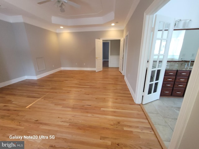 empty room with ceiling fan, ornamental molding, a tray ceiling, and light hardwood / wood-style floors