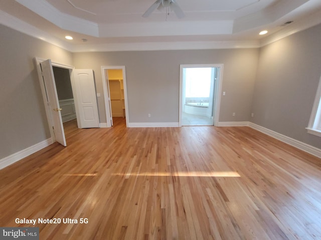 unfurnished room with crown molding, a raised ceiling, ceiling fan, and light wood-type flooring