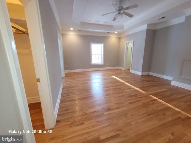 spare room with a raised ceiling, ceiling fan, ornamental molding, and light hardwood / wood-style floors