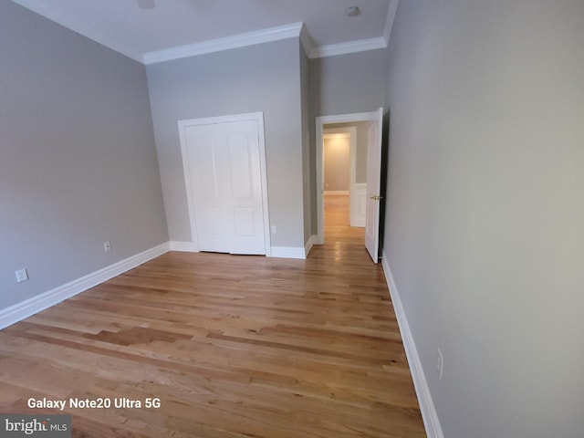 unfurnished bedroom featuring crown molding, light hardwood / wood-style floors, and a closet