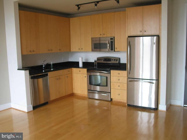 kitchen with sink, light brown cabinets, track lighting, appliances with stainless steel finishes, and light hardwood / wood-style floors