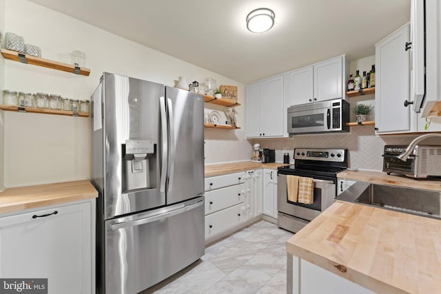 kitchen with appliances with stainless steel finishes, butcher block counters, sink, white cabinets, and decorative backsplash