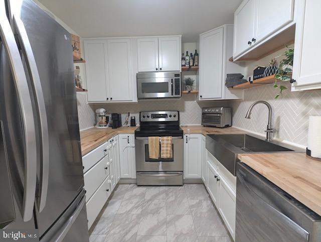 kitchen featuring white cabinetry, wood counters, appliances with stainless steel finishes, and sink