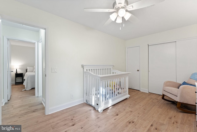 bedroom with a nursery area, ceiling fan, and light wood-type flooring