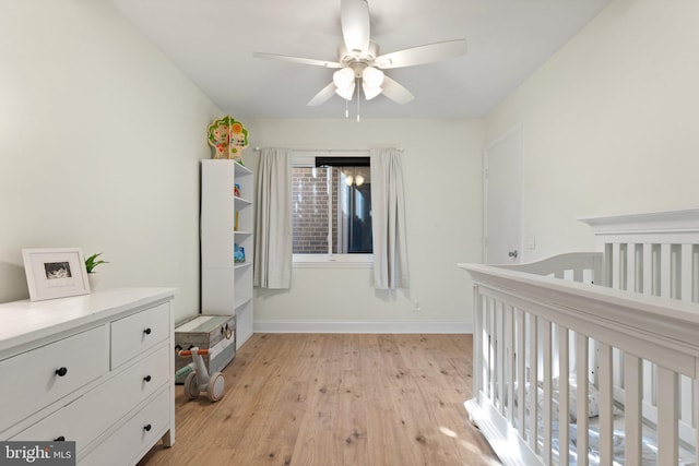 bedroom featuring ceiling fan, light hardwood / wood-style flooring, and a crib