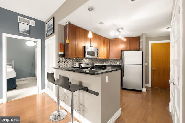 kitchen with hardwood / wood-style flooring, a kitchen breakfast bar, pendant lighting, stainless steel appliances, and decorative backsplash