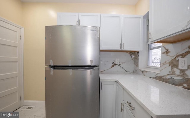 kitchen featuring stainless steel refrigerator, light stone countertops, and white cabinets