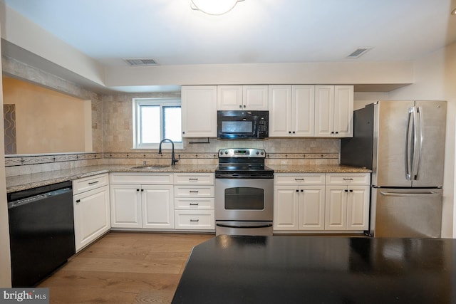 kitchen with sink, white cabinets, decorative backsplash, black appliances, and light hardwood / wood-style flooring