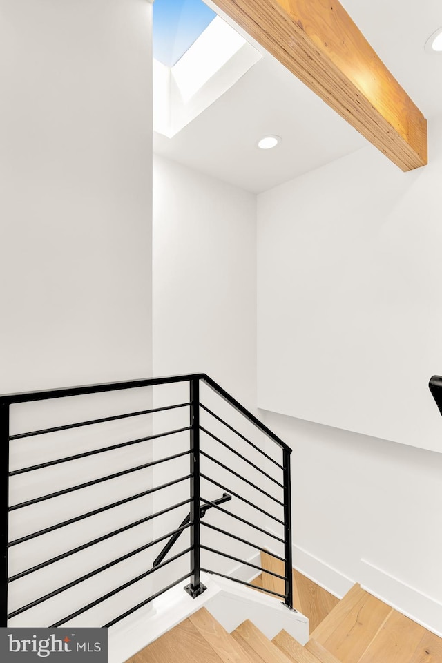 staircase featuring beam ceiling, a skylight, and hardwood / wood-style floors