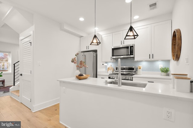 kitchen featuring white cabinetry, tasteful backsplash, hanging light fixtures, light wood-type flooring, and stainless steel appliances