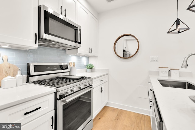 kitchen featuring appliances with stainless steel finishes, pendant lighting, sink, white cabinets, and decorative backsplash