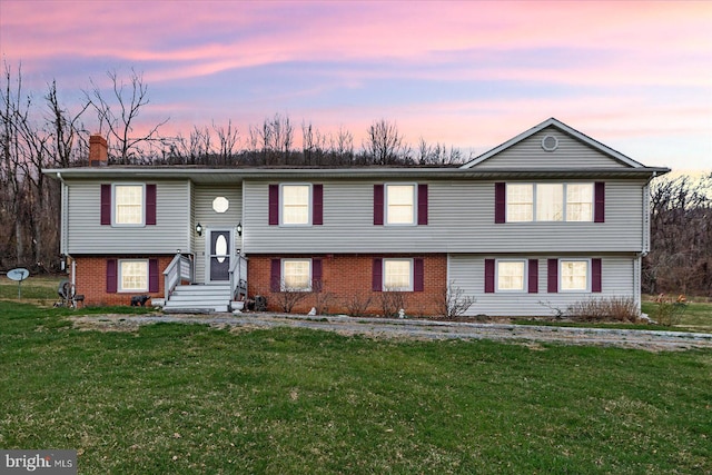 bi-level home featuring a chimney, brick siding, and a yard