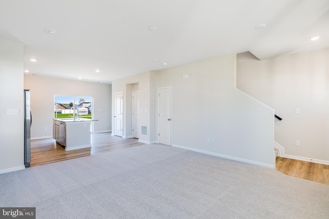 unfurnished living room featuring sink and light carpet