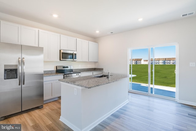 kitchen featuring sink, appliances with stainless steel finishes, white cabinetry, light stone counters, and an island with sink