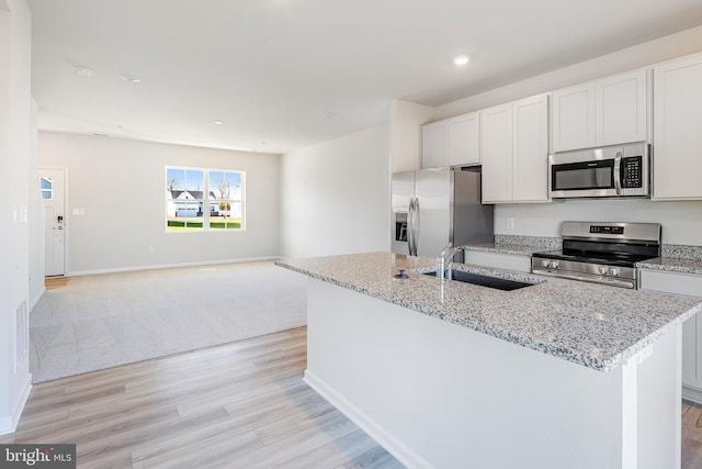 kitchen with stainless steel appliances, white cabinetry, a kitchen island with sink, and light stone counters