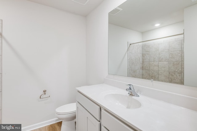 bathroom with hardwood / wood-style flooring, vanity, a tile shower, and toilet