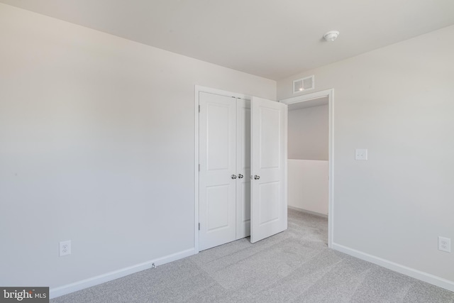 unfurnished bedroom with light colored carpet and a closet