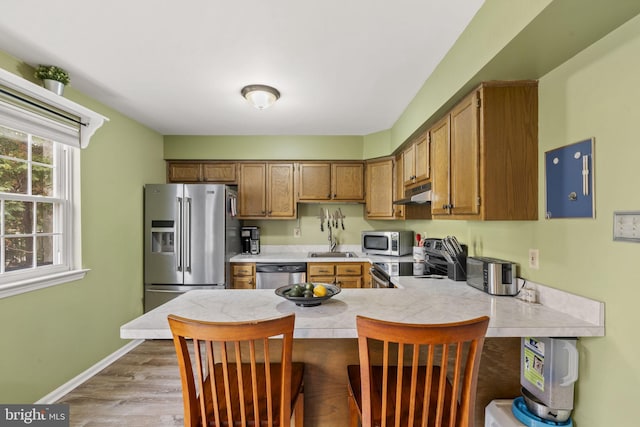 kitchen with sink, light wood-type flooring, a kitchen breakfast bar, kitchen peninsula, and stainless steel appliances