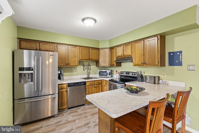 kitchen featuring a kitchen bar, sink, light hardwood / wood-style flooring, kitchen peninsula, and stainless steel appliances