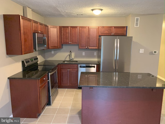 kitchen featuring light tile patterned flooring, appliances with stainless steel finishes, sink, dark stone counters, and a textured ceiling