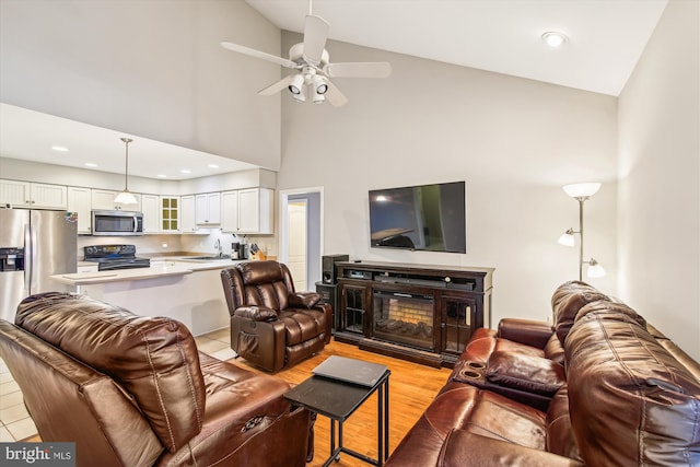 living room featuring sink, high vaulted ceiling, ceiling fan, and light wood-type flooring