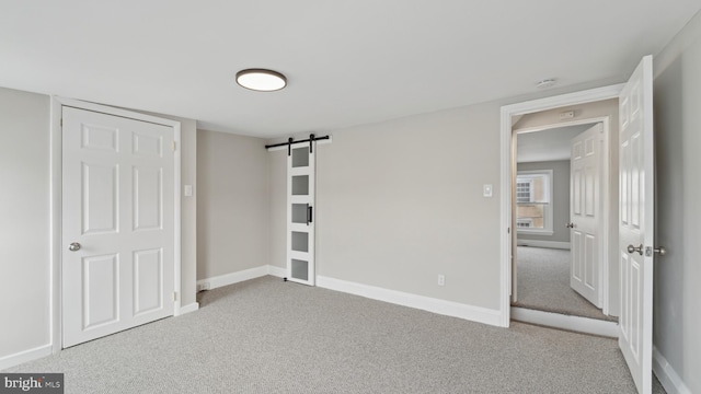 unfurnished bedroom with a barn door and light carpet