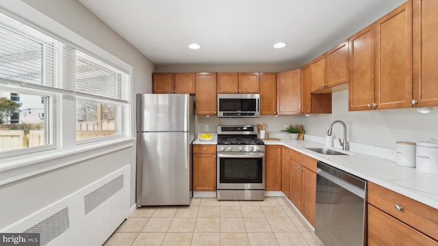 kitchen with stainless steel appliances, light tile patterned flooring, light stone countertops, and sink