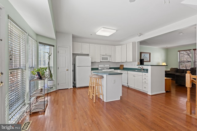 kitchen with a breakfast bar area, a center island, light hardwood / wood-style flooring, white appliances, and white cabinets