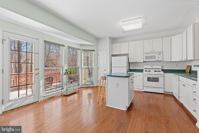 kitchen featuring hardwood / wood-style flooring, a breakfast bar area, white cabinets, and white appliances