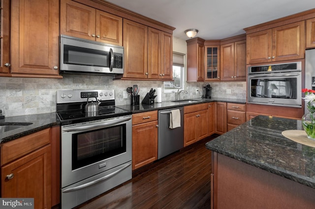 kitchen with sink, dark stone countertops, appliances with stainless steel finishes, dark hardwood / wood-style floors, and backsplash