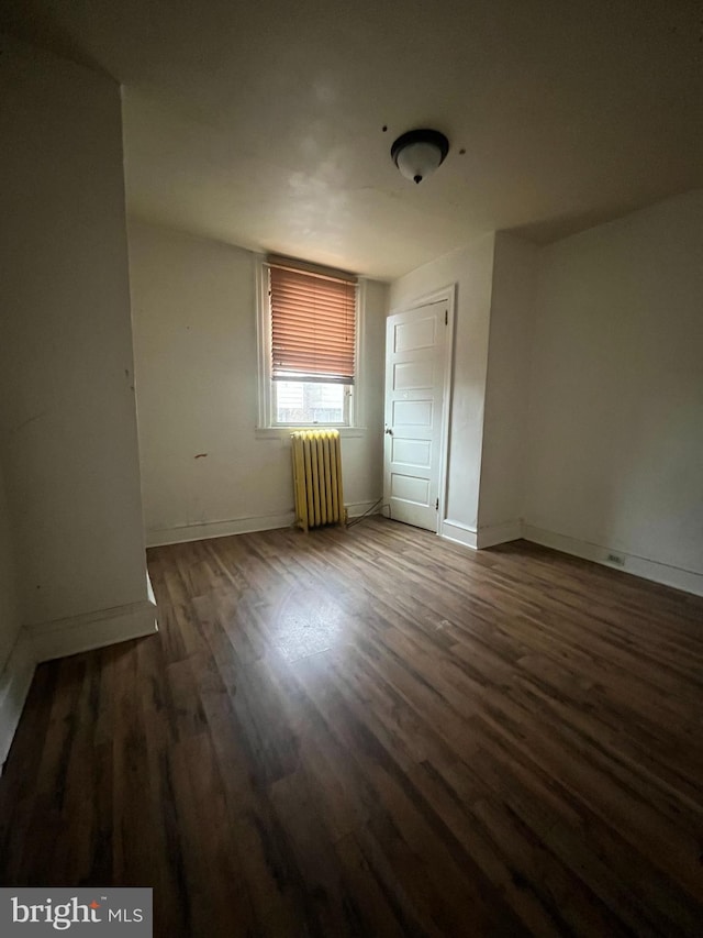 empty room with dark wood-type flooring and radiator