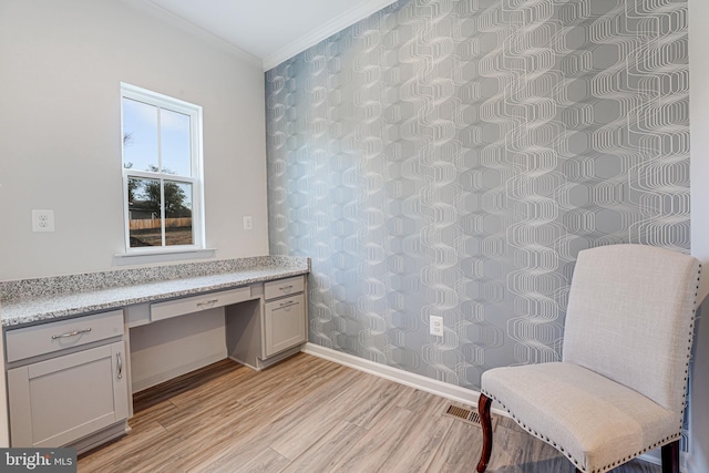 unfurnished room featuring crown molding, built in desk, and light hardwood / wood-style floors