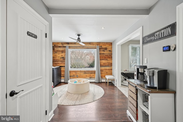 living area featuring dark wood-type flooring, ceiling fan, and wood walls