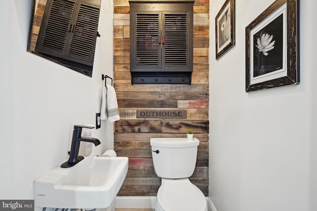 bathroom featuring sink, toilet, and wood walls