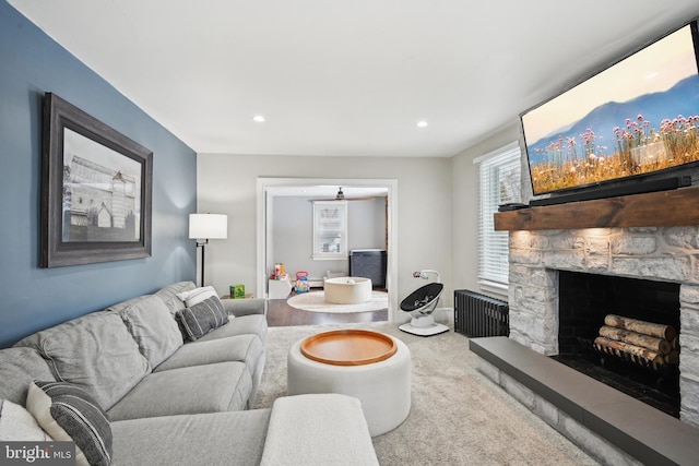 living room with carpet floors, a stone fireplace, and radiator