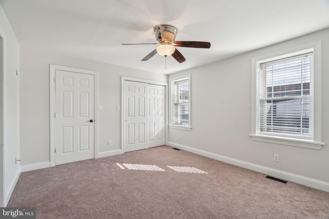 unfurnished bedroom with multiple closets, ceiling fan, and light colored carpet