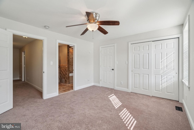 unfurnished bedroom featuring light carpet, multiple closets, ensuite bath, and ceiling fan